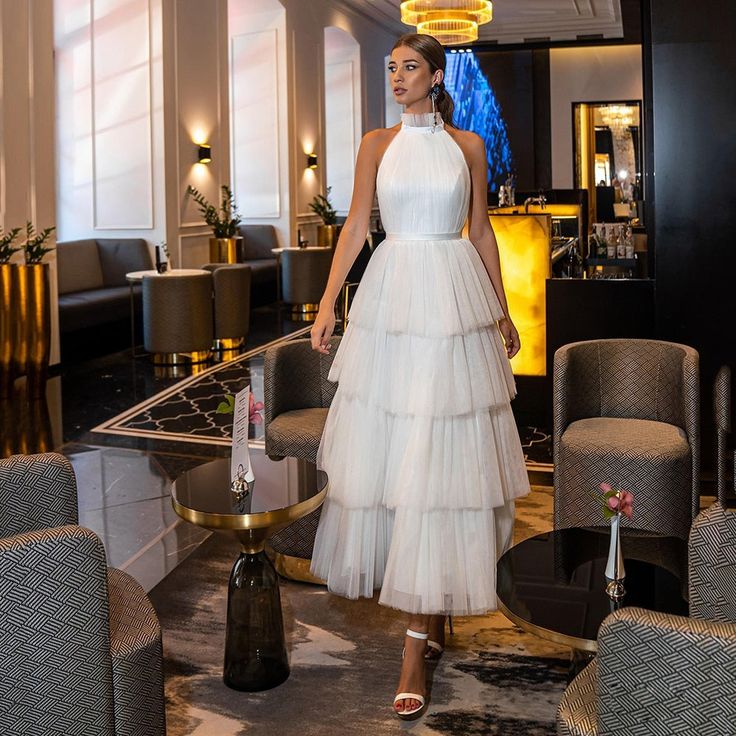 a woman in a white dress standing next to a table with chairs and tables behind her