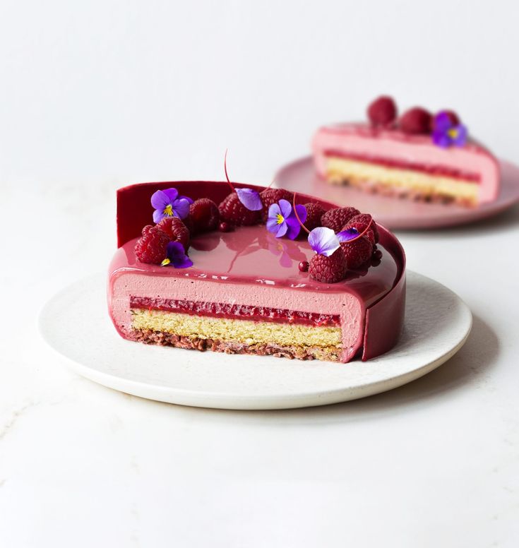 a piece of cake with raspberries and purple flowers on it sitting on a plate