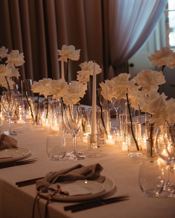 there are many flowers in vases on the table with candles and place settings around them