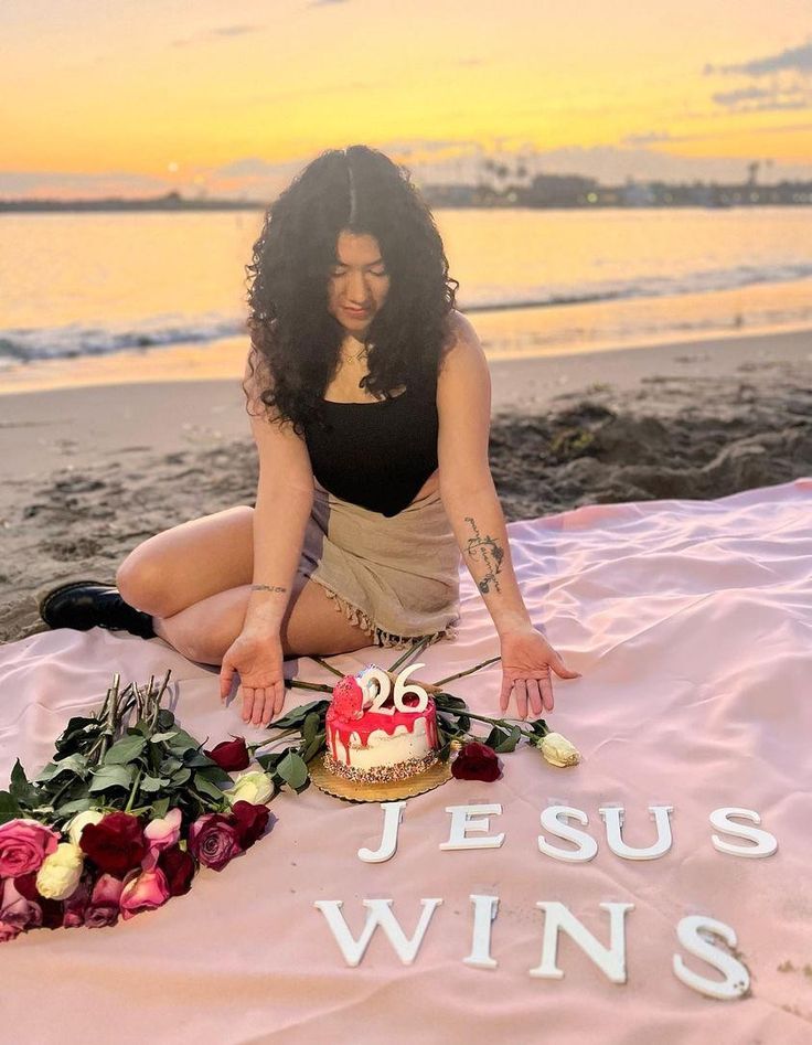 a woman sitting on top of a blanket with a cake in front of her and the words jesus wins