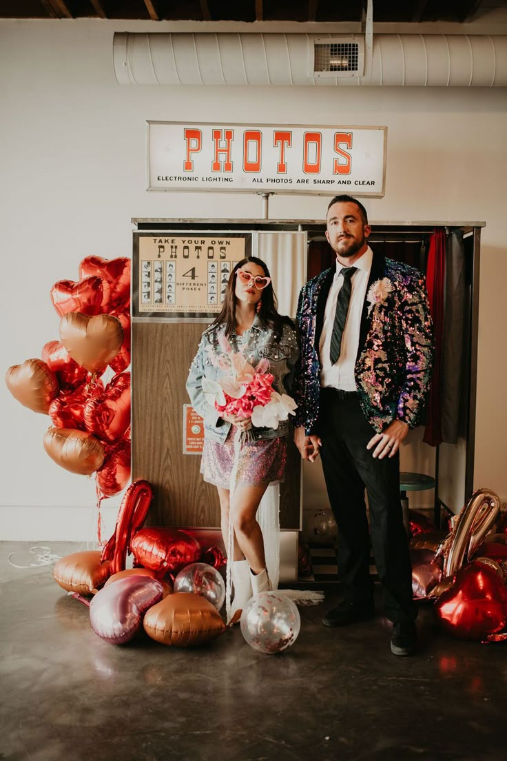 a man and woman standing next to each other in front of an assortment of balloons