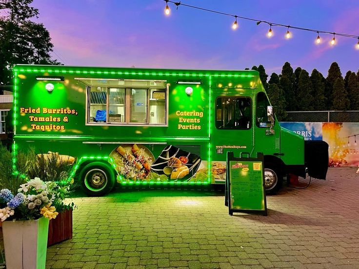 a green food truck parked in front of a building with string lights on the roof