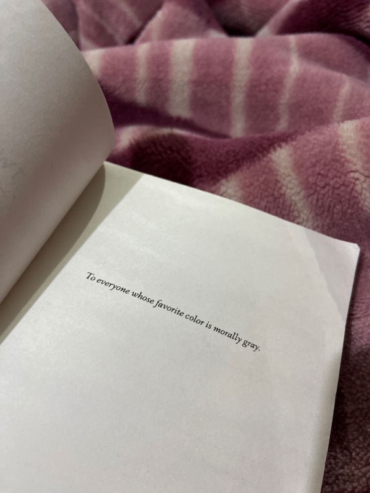 an open book laying on top of a bed next to a pink and white blanket