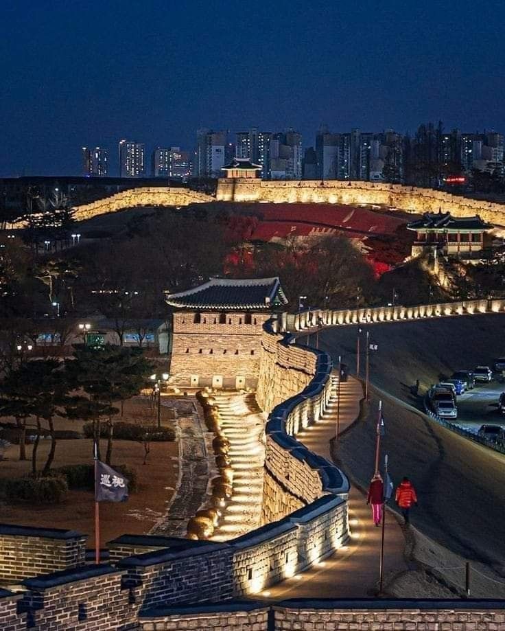 the city lights shine brightly in the night sky over an old stone wall with steps leading up to it