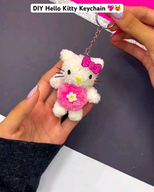 a person holding a hello kitty keychain with a pink bow on it's neck