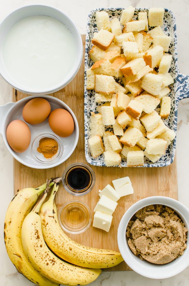 ingredients to make banana bread laid out on a cutting board, including eggs, butter, sugar and milk