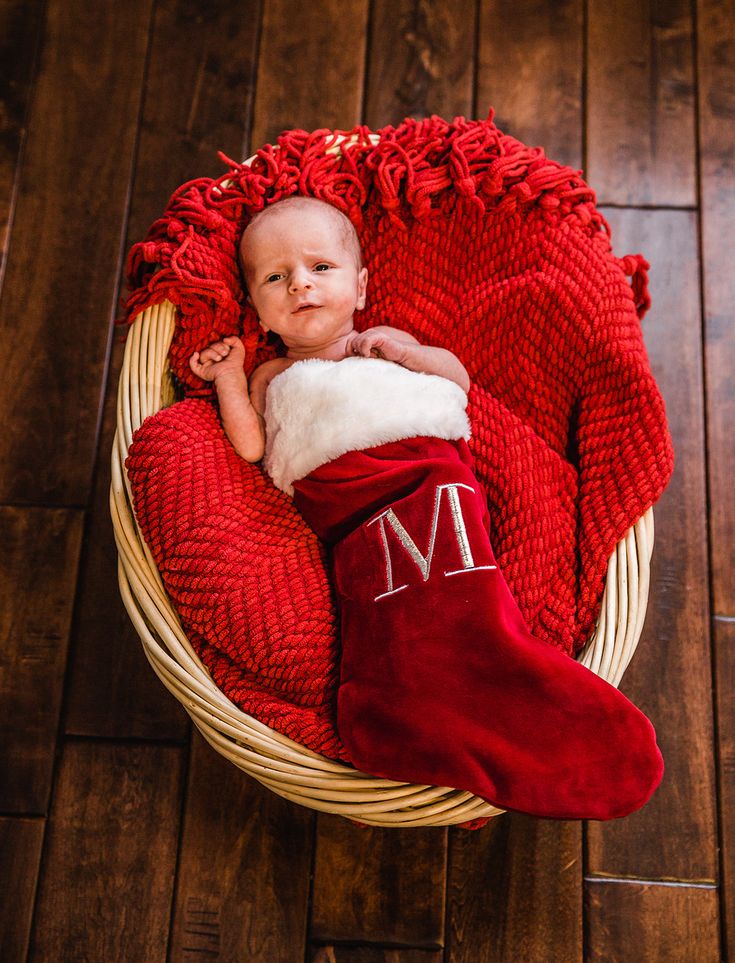 a baby wrapped in a red blanket and wearing a christmas stocking on top of a wooden floor