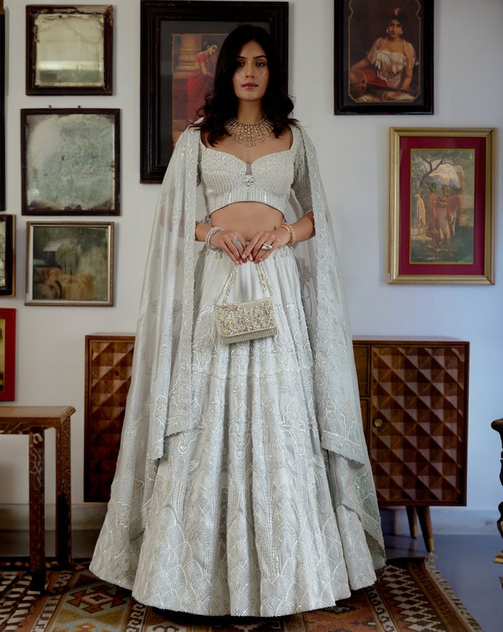 Divine is what comes to one’s mind while seeing up this moonlit beauty. Adorned with the purity of white tone and the hand-printed motifs embellished with white crystal beads and pearl moti sets up the ethereal mood for the celebrations. A perfect blend of modernity and tradition curated for the modern Indian brides.• Elbow-length blouse with a sweetheart neckline adorned with white pearl moti, crystal beads, and mirror-work. • Blouse contains a zip along with a metal hook on the left side.• The flowy translucent white embroidered dupatta with embroidered border. • The hand-printed motifs adorn the lehenga skirt embellished with handcrafted embroidery highlighting the motifs. • Lehenga contains a left zipper for support.From Moledro’s Fitoor collection. DELIVERY TIMEPlease allow 8-12 weeks Elegant Set With Pearl Embroidery For Reception, Elegant Sets With Pearl Embroidery For Reception, Designer White Lehenga With Pearl Embroidery, Designer Pearl Embroidered Elegant Lehenga, Elegant Designer Lehenga With Pearl Embroidery, Elegant Off White Lehenga For Festive Occasions, Designer Pearl Embroidery Lehenga, White Hand-embellished Sets With Traditional Drape, White Hand Embellished Sets With Traditional Drape