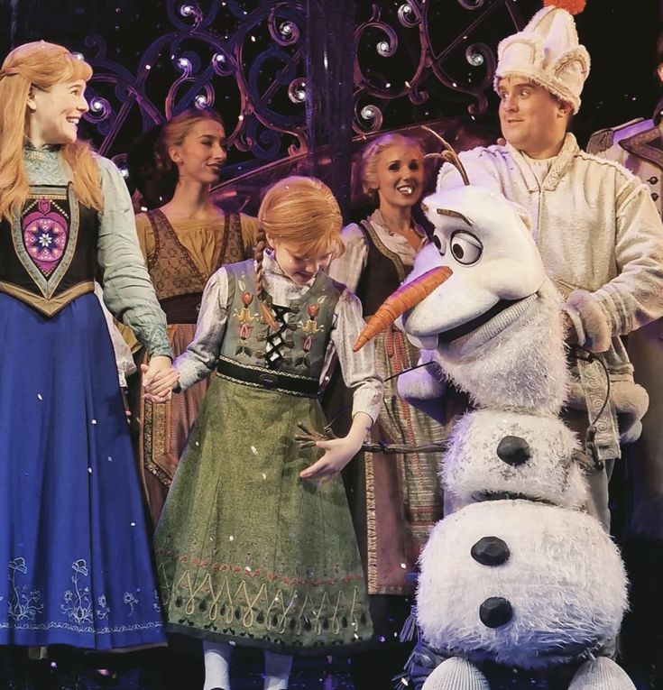 a group of people standing next to each other in front of a frozen princess costume