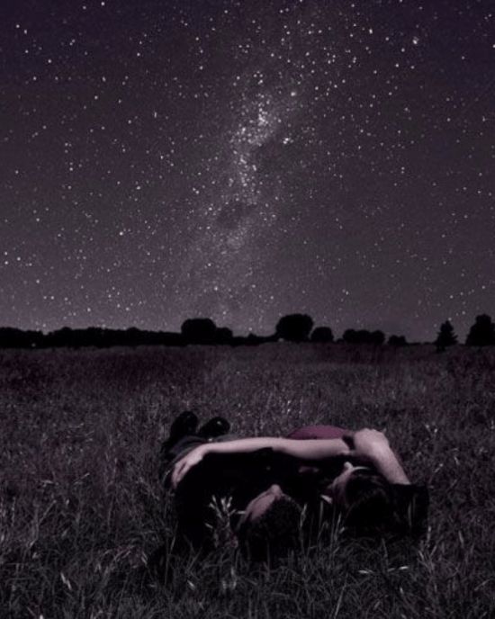 a person laying in the grass under a night sky filled with stars