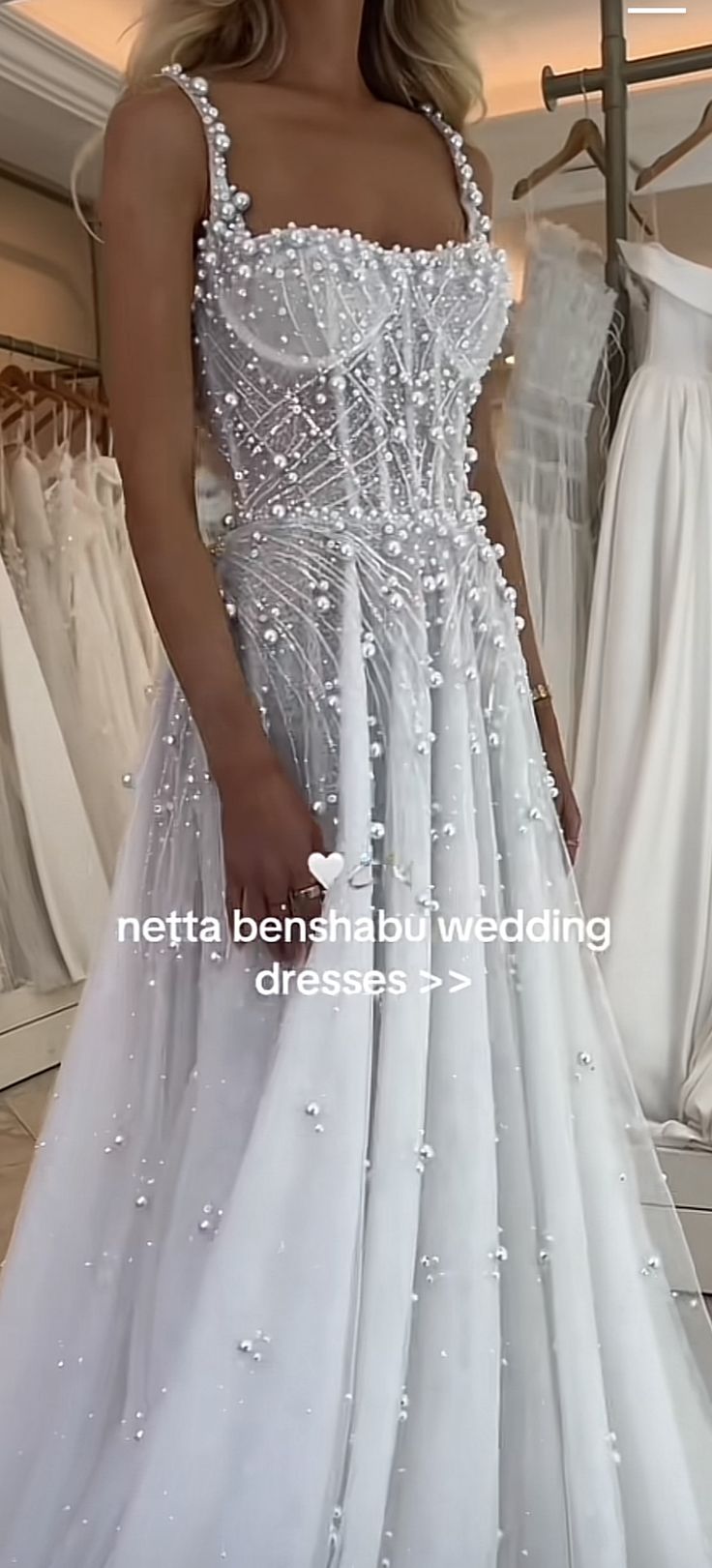 a woman in a white dress standing next to a rack of wedding gowns and dresses