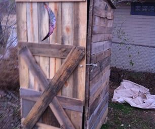 an outhouse made from wood with a door open and a cat in the yard