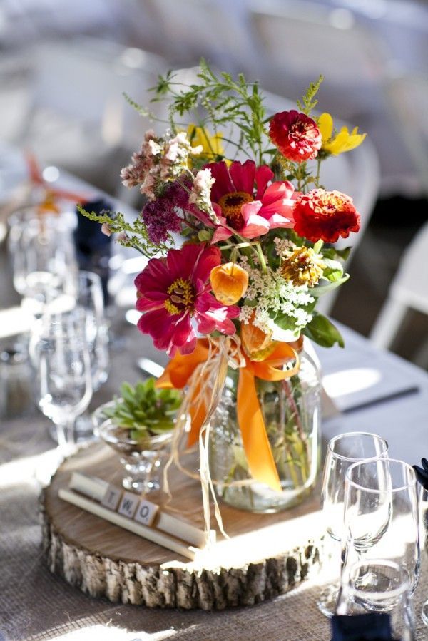 a vase filled with colorful flowers sitting on top of a wooden table next to wine glasses