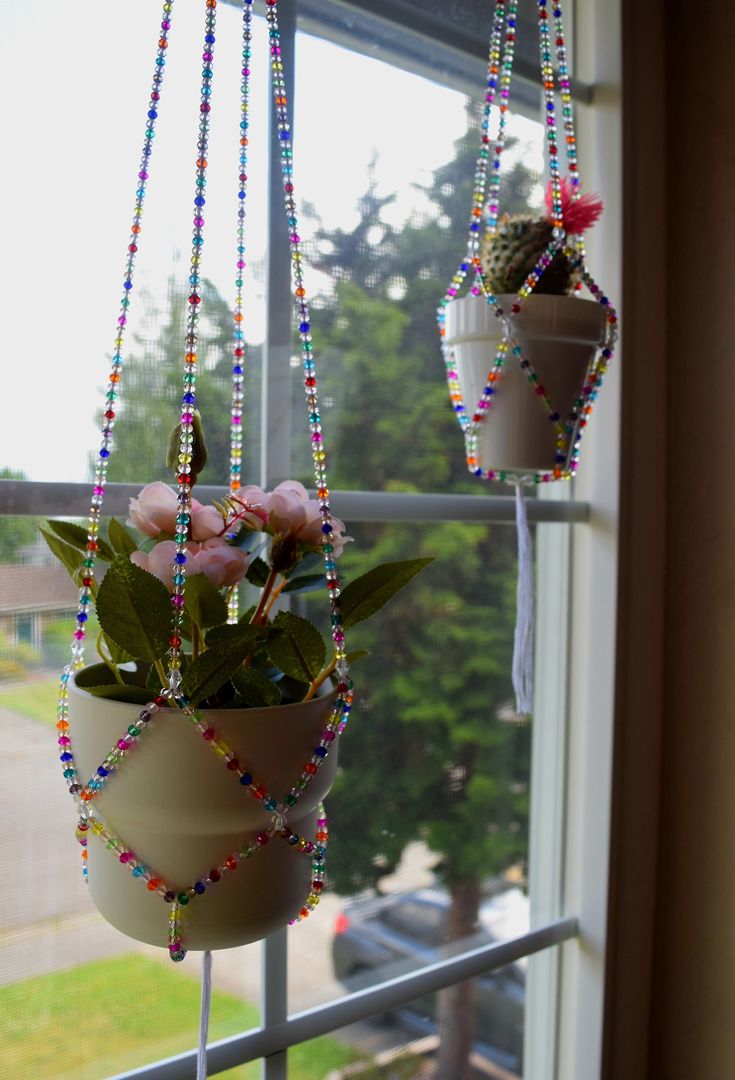 two potted plants hanging from a window sill with beads and flowers in them