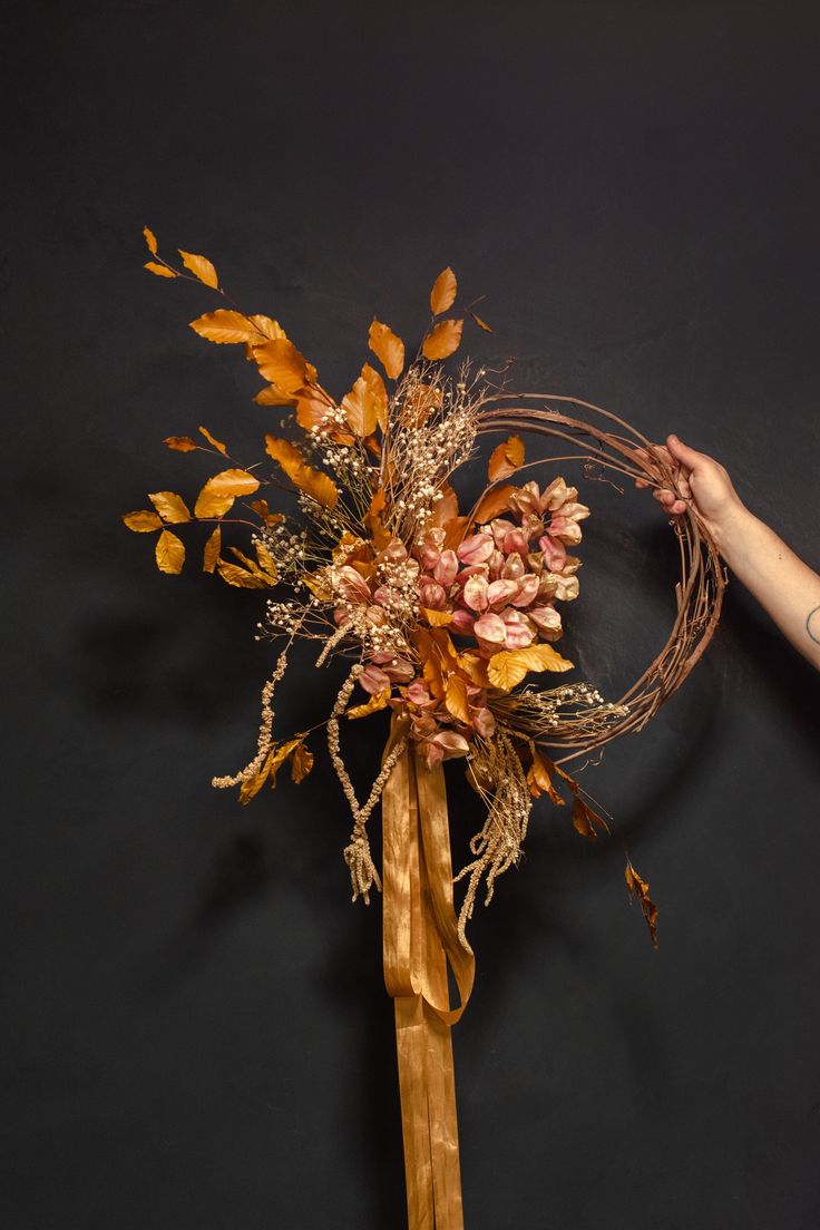 a bouquet of dried flowers is being held by a woman's hand on a black background