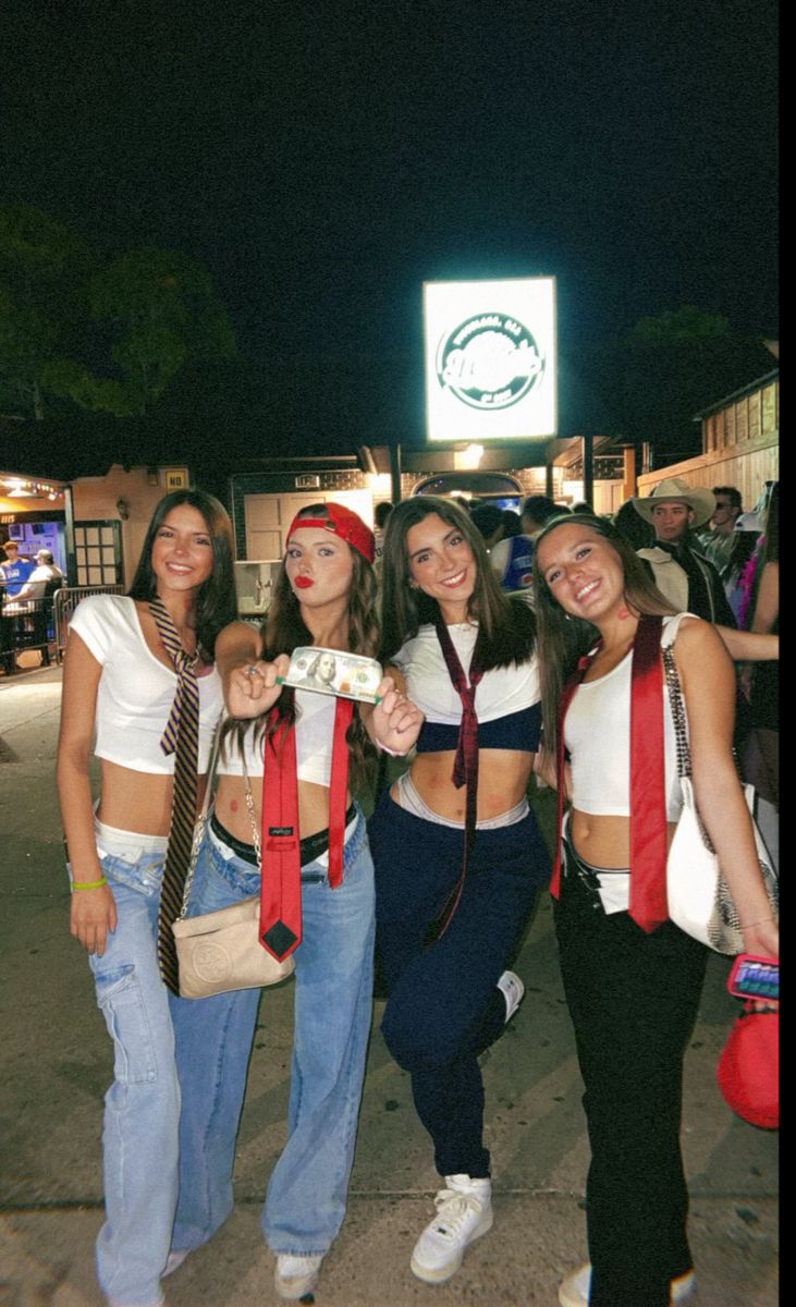 four girls are posing for the camera in front of a building at night with their ties around their waist