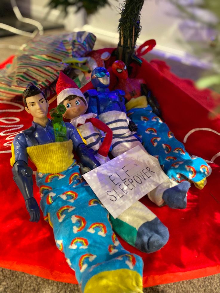 two elf dolls sitting on top of a red blanket next to a christmas tree with an ornament