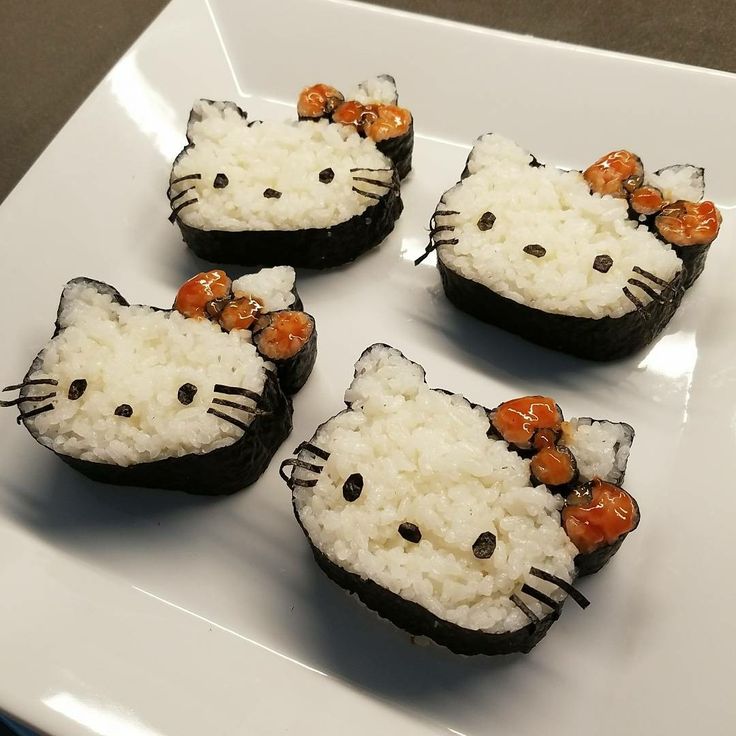 four hello kitty rice cakes on a white plate with carrots in the shape of cats