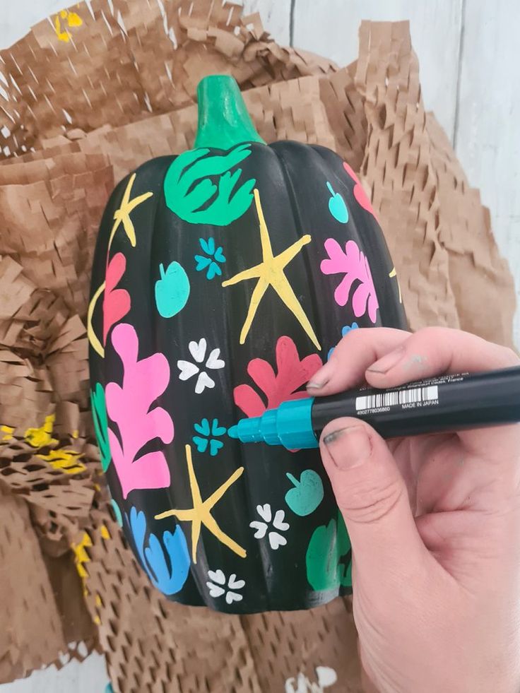 a hand holding a marker near a painted pumpkin