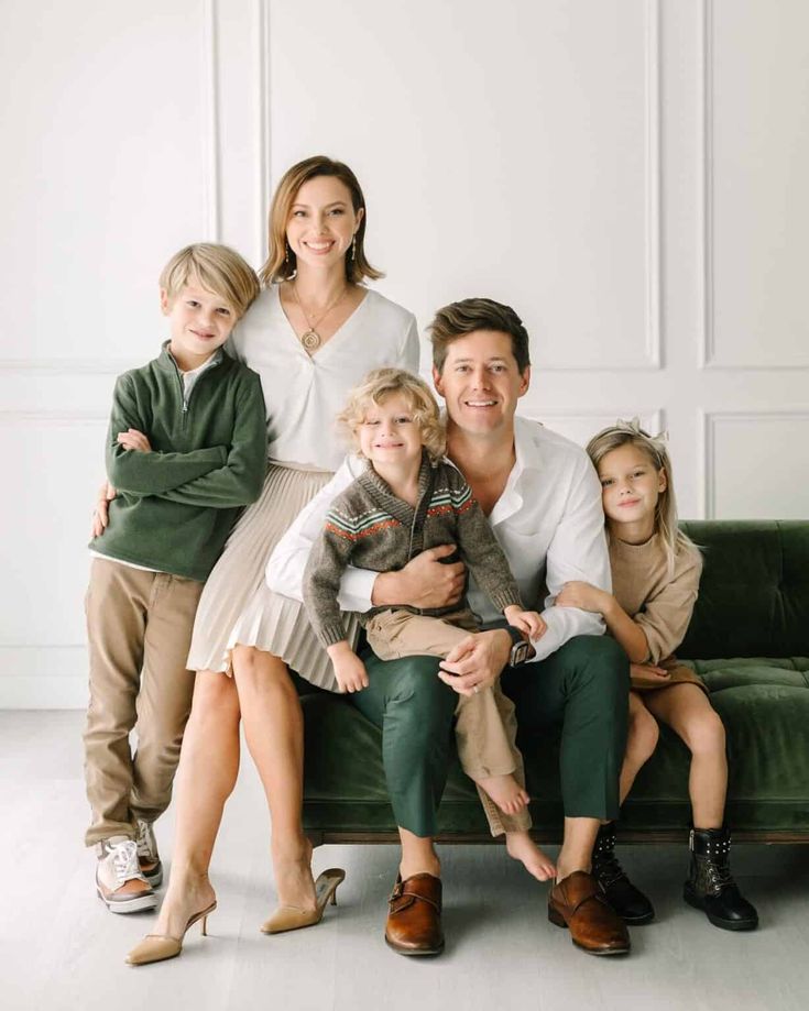 a family sitting on a green couch in front of a white wall with their arms around each other