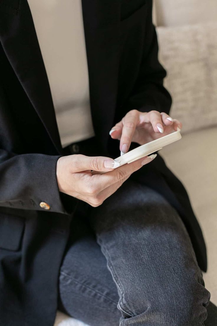 a person sitting on a couch holding a cell phone in one hand and looking at the other