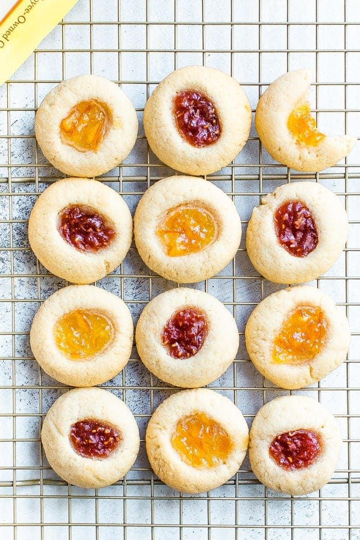 several cookies with jam on them sitting on a cooling rack next to an orange peel