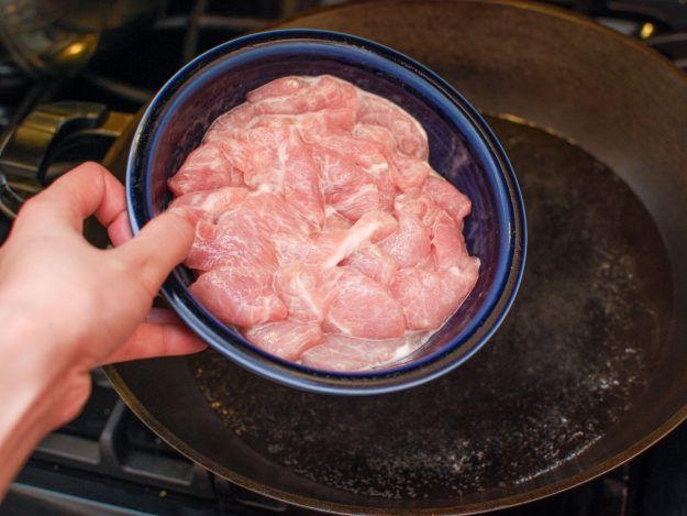 a person holding a blue bowl filled with raw meat on top of a stovetop