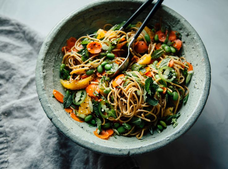 a bowl filled with noodles and vegetables on top of a gray cloth next to a fork