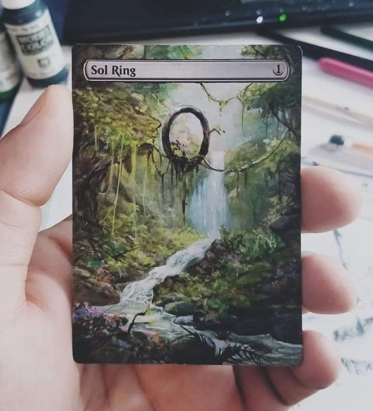 a person holding up a card with a waterfall in the middle and trees on it