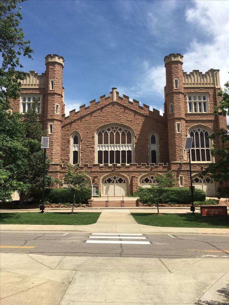 an old brick building with two towers and large windows on the front, surrounded by green grass and trees