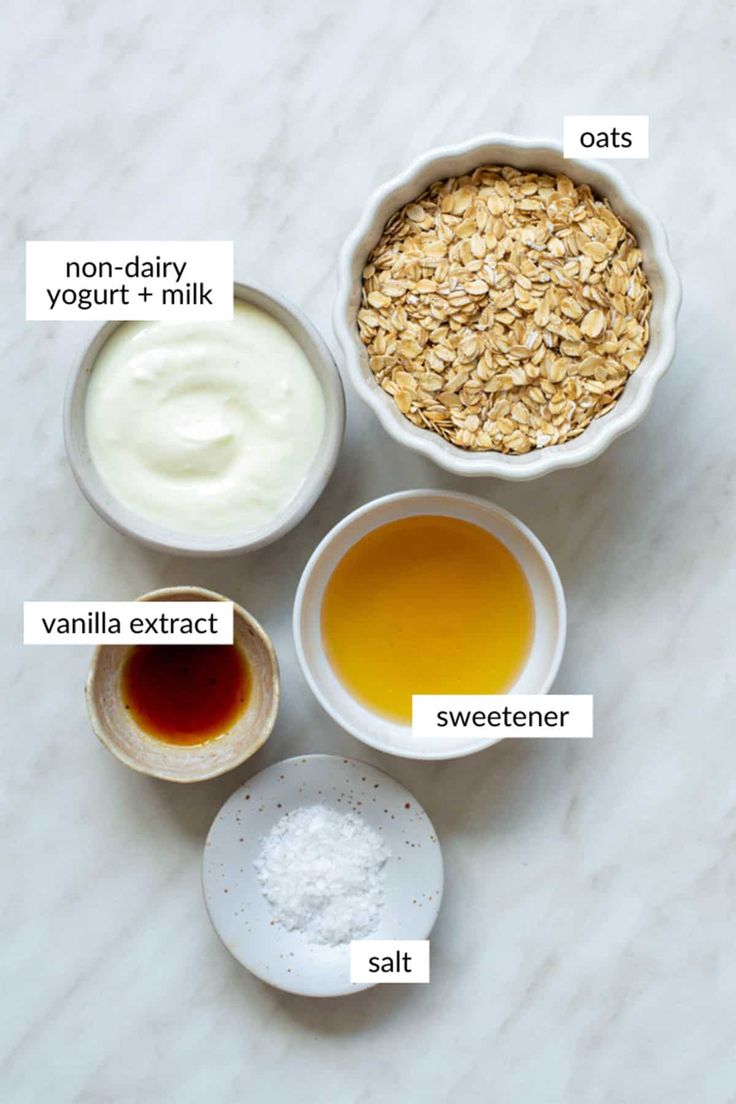 ingredients to make oatmeal in small bowls on a marble countertop with labels