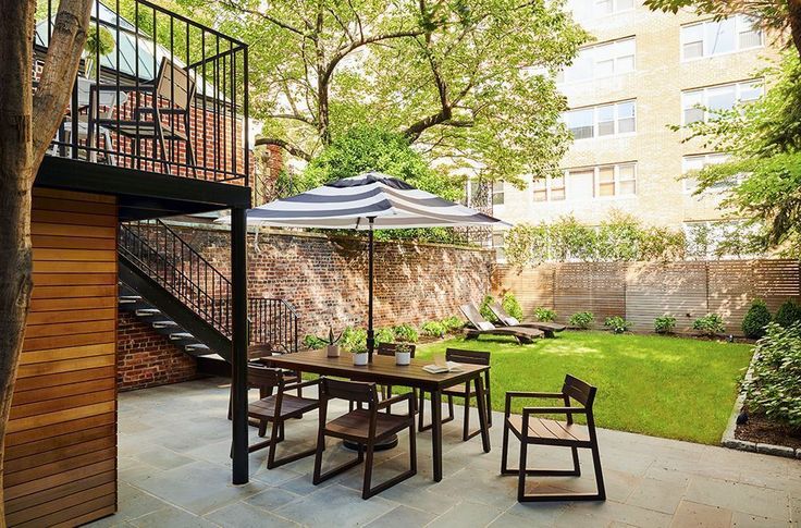 an outdoor dining area with patio furniture and umbrella over the table, surrounded by trees