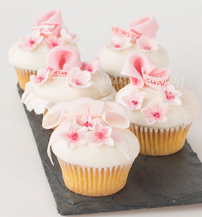 several cupcakes with white frosting and pink flowers on top are sitting on a black tray