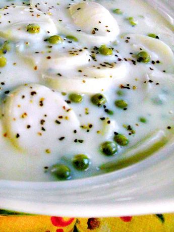 a white bowl filled with peas and cream on top of a yellow table cloth next to an orange napkin