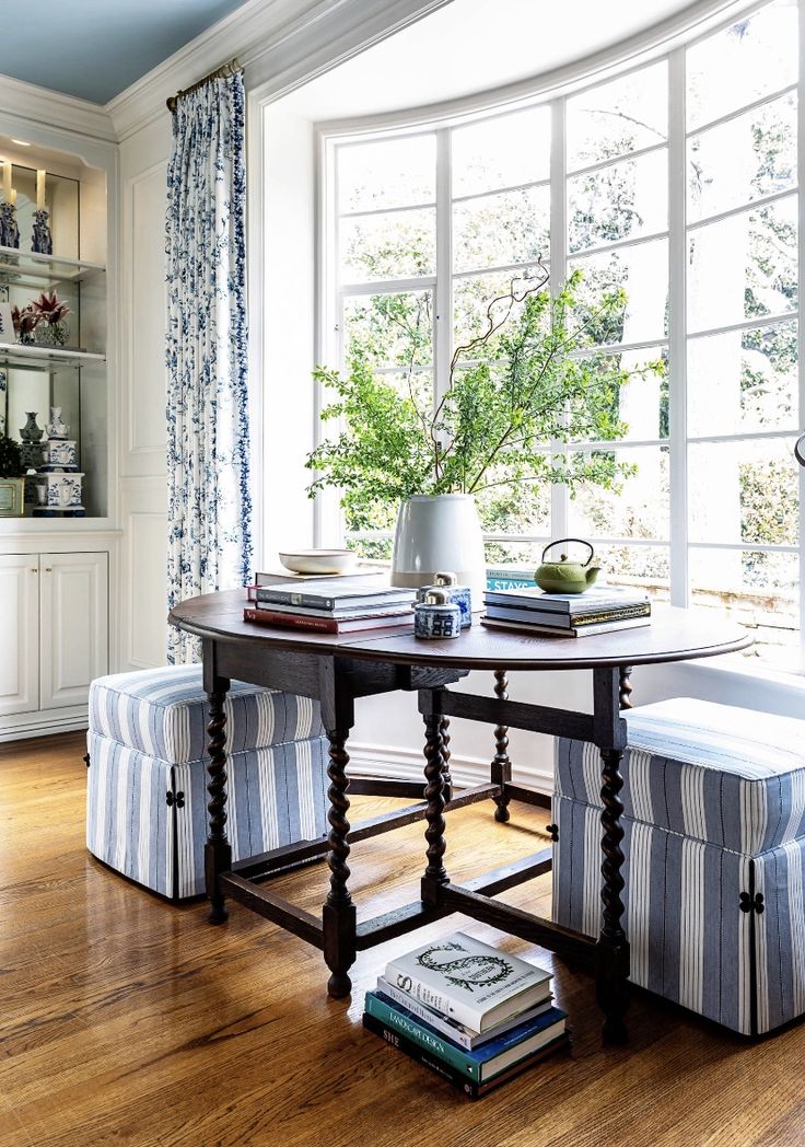 a dining room table in front of a window with blue and white curtains on the windowsill