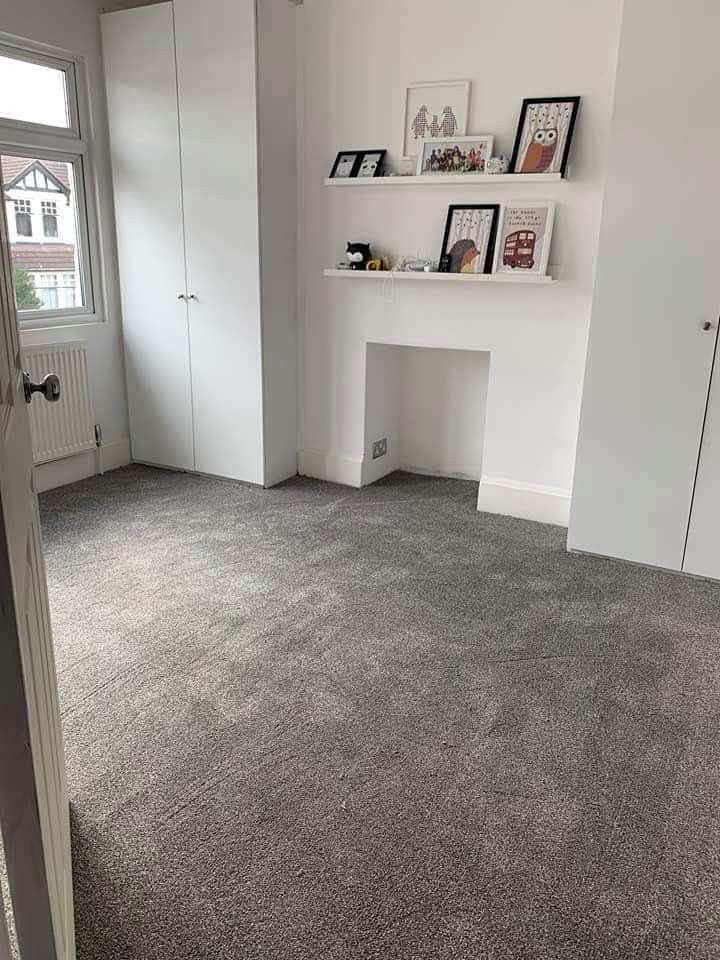 an empty room with white walls and gray carpeted flooring is seen in this image