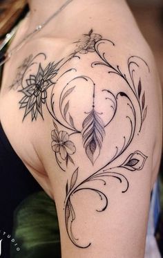 the back of a woman's shoulder with flowers and leaves tattoo on her left arm