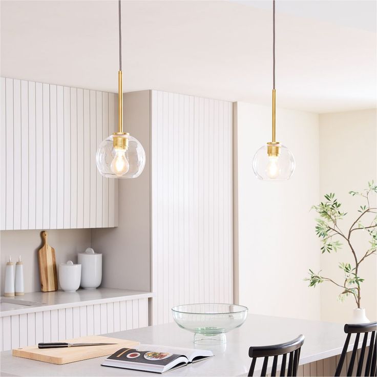 a kitchen with white cabinets and yellow fruit on the counter top in front of two pendant lights