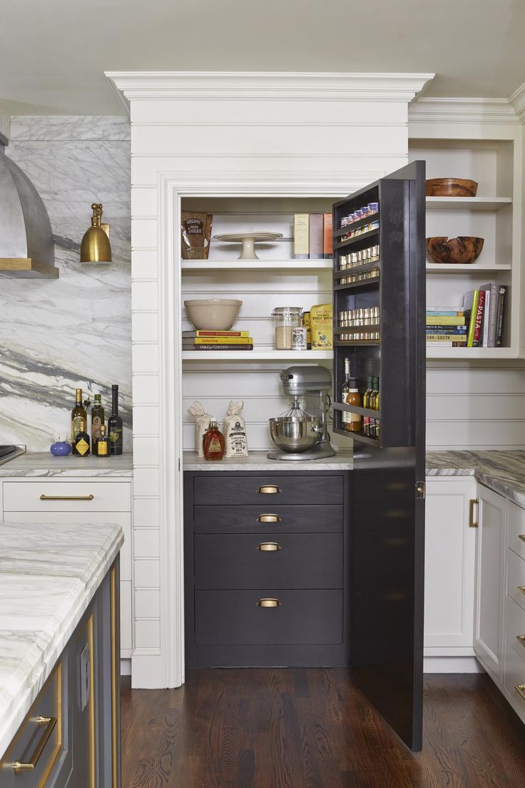 a kitchen with white cabinets and marble counter tops, along with brass pulls on the doors