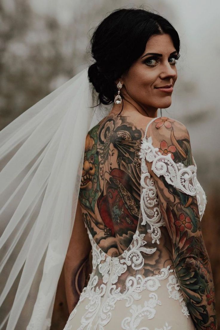 a woman with tattoos on her back and veil over her shoulder is looking at the camera