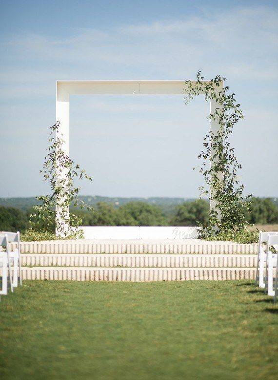 an outdoor ceremony setup with white chairs and greenery