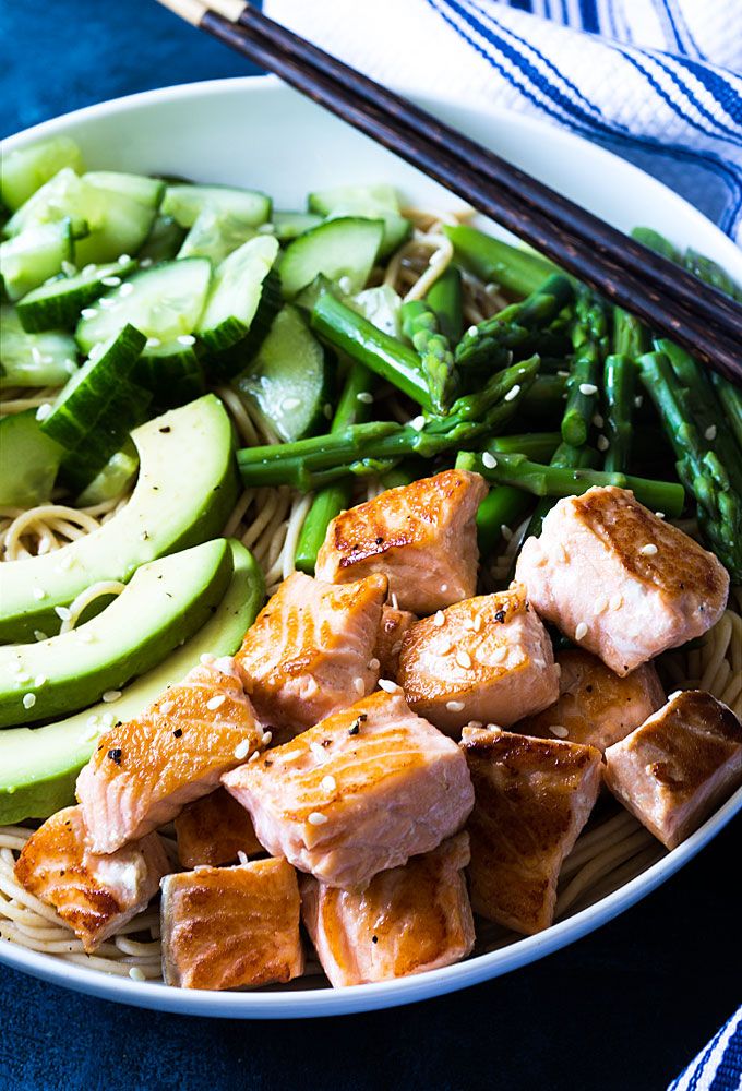 a white bowl filled with meat and veggies next to chopsticks on a blue table cloth