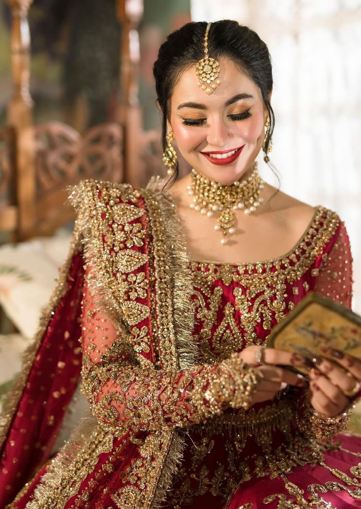 a woman in a red and gold bridal outfit smiles while holding an open book