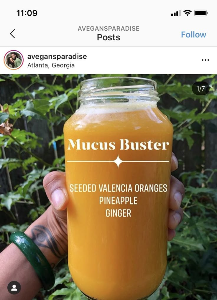 a person holding up a mason jar filled with orange juice and labeled mucus buster