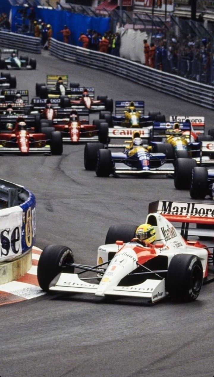 a group of racing cars driving around a track with people watching from the sidelines