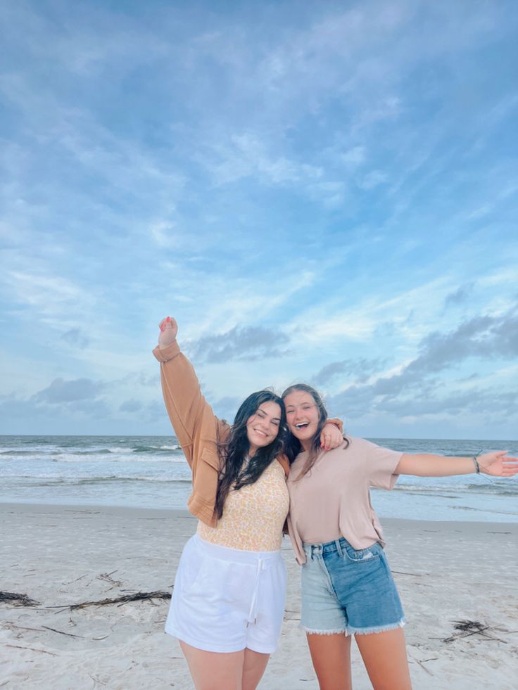 two women standing on the beach with their arms in the air