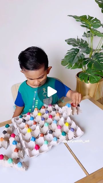 a little boy sitting at a table with an egg carton