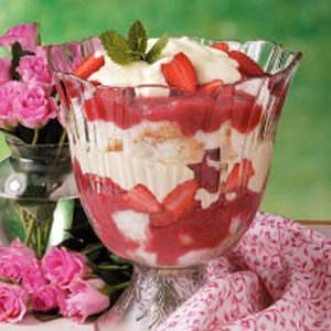 a dessert with strawberries and whipped cream in a glass bowl next to pink flowers