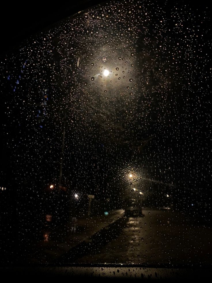 rain drops on the window at night with street lights and cars parked in the background