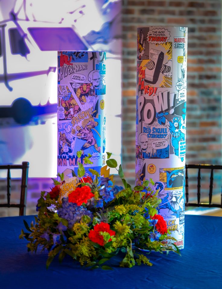 two tall vases with flowers on top of a blue table cloth covered table in front of a brick wall